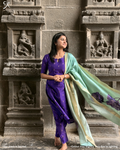 Woman wearing violet raw silk salwar set with pastel muslin dupatta near temple wall