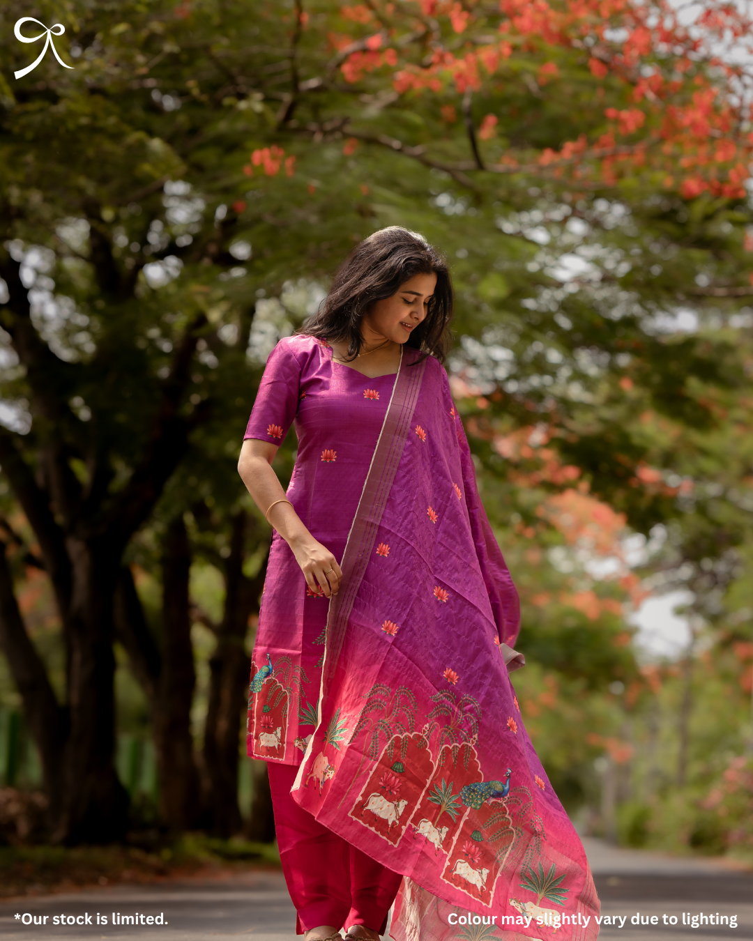 Woman in a purple traditional outfit with floral patterns standing outdoors with trees in the background.
